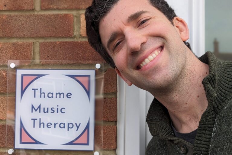 Hugh stands in front of Thame Music Therapy sign