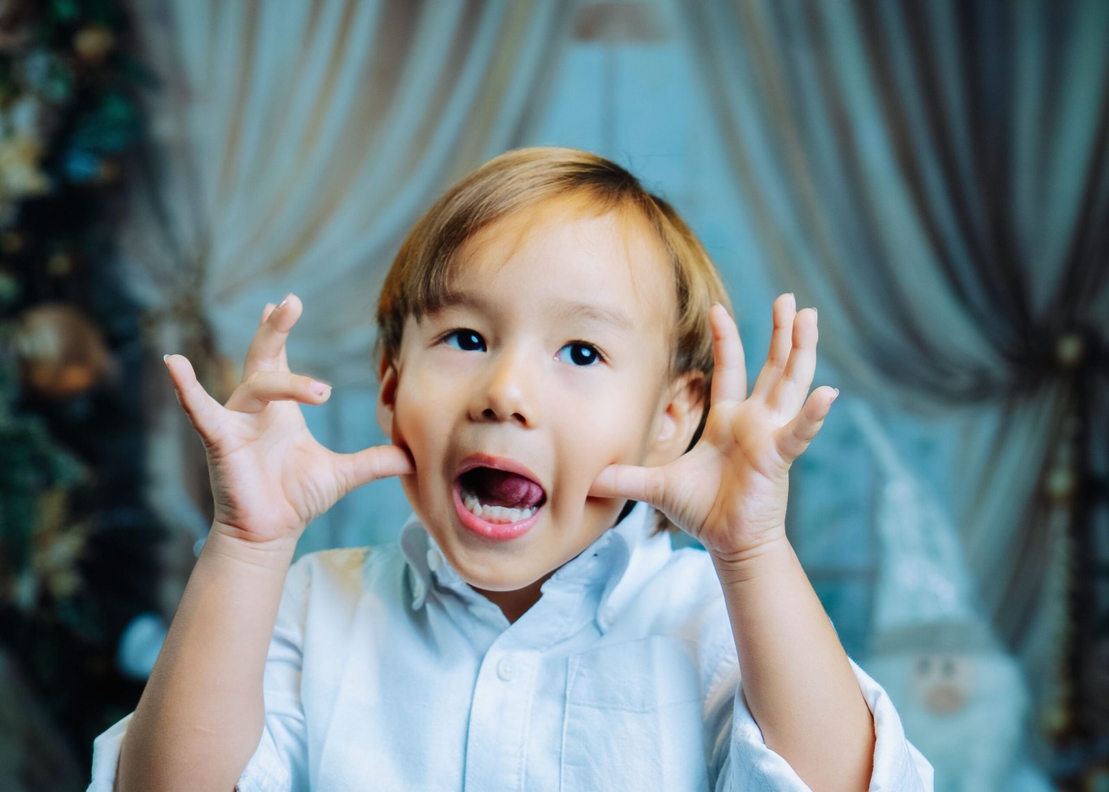 A playful child in a white shirt making funny faces indoors with a blurred background.